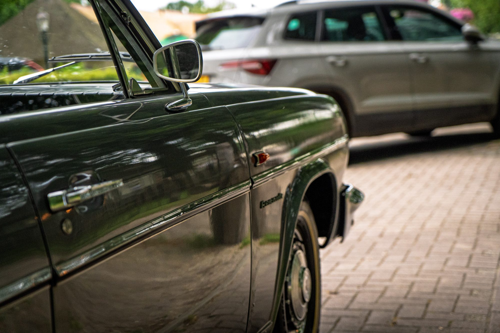 Zijkant van een klassieke donkergroene auto op een klinkerweg